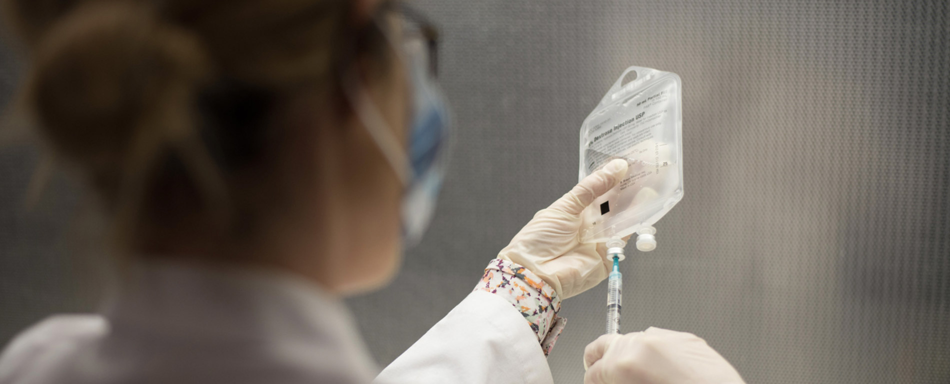 clinical lab person with syringe drawing fluid from a clear bag