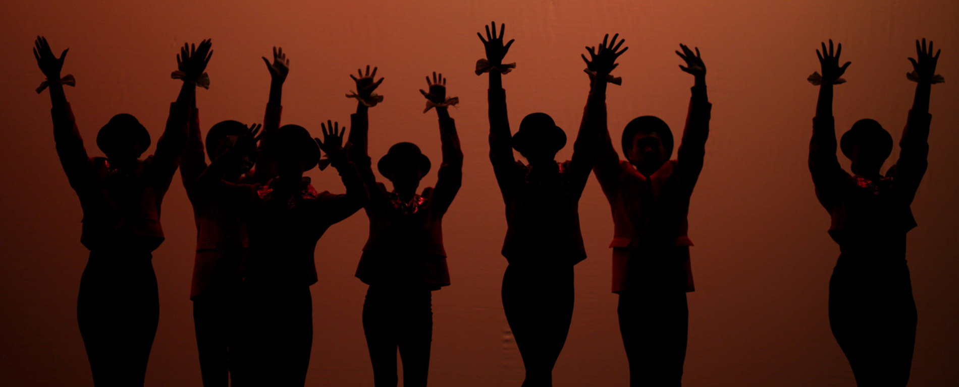 dancers in shadow against a brighter background with hands raised