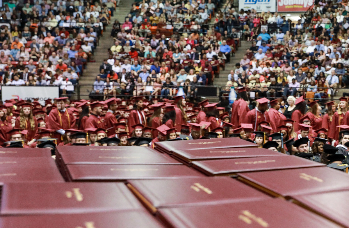 ULM degrees stacked on a table ready to be presented, students and audience seated in the background