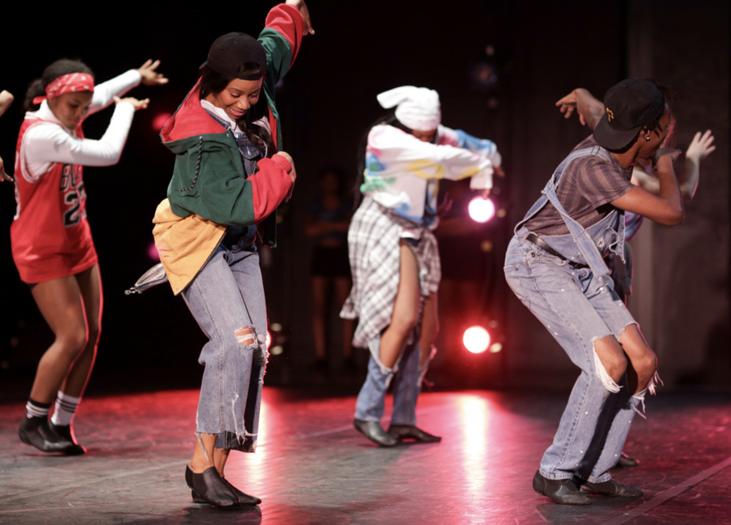 Four dancers in various costumes perform on stage in Brown Auditorium.