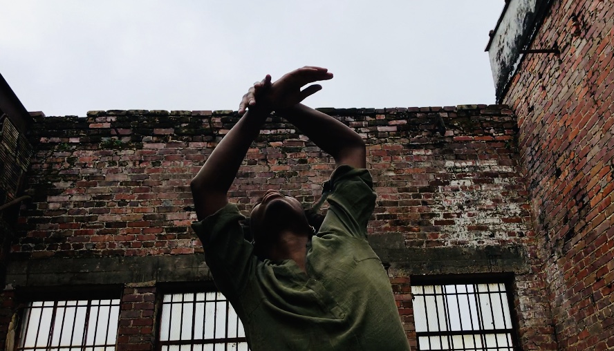 A solo dancer performs in front of an old brick building underneath the open sky.