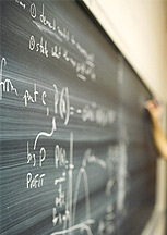 hand at chalkboard complex mathematical equations written in chalk on a blackboard