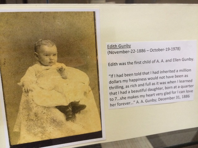 The displayed photograph features a child, identified as Edith Gunby. Edith lived from November 22, 1886 to October 19, 1978. Edith was the first child of A.A. and Ellen Gunby, and includes a touching quote from her father, A.A. Gunby, written on December 31, 1886, expressing his joy at her birth: "If I had been told that I had inherited a million dollars my happiness would not have been as thrilling, as rich and full as it was when I learned that I had a beautiful daughter, born at a quarter to 7...she makes my heart very glad for I can love her forever..."