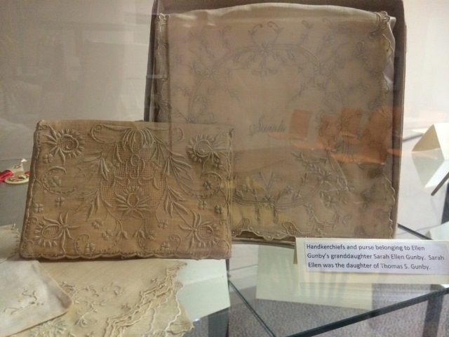 The image displays a collection of handkerchiefs and a purse belonging to Sarah Ellen Gunby. Sarah Ellen Gunby was the granddaughter of Ellen Gunby and the daughter of Thomas Gunby.