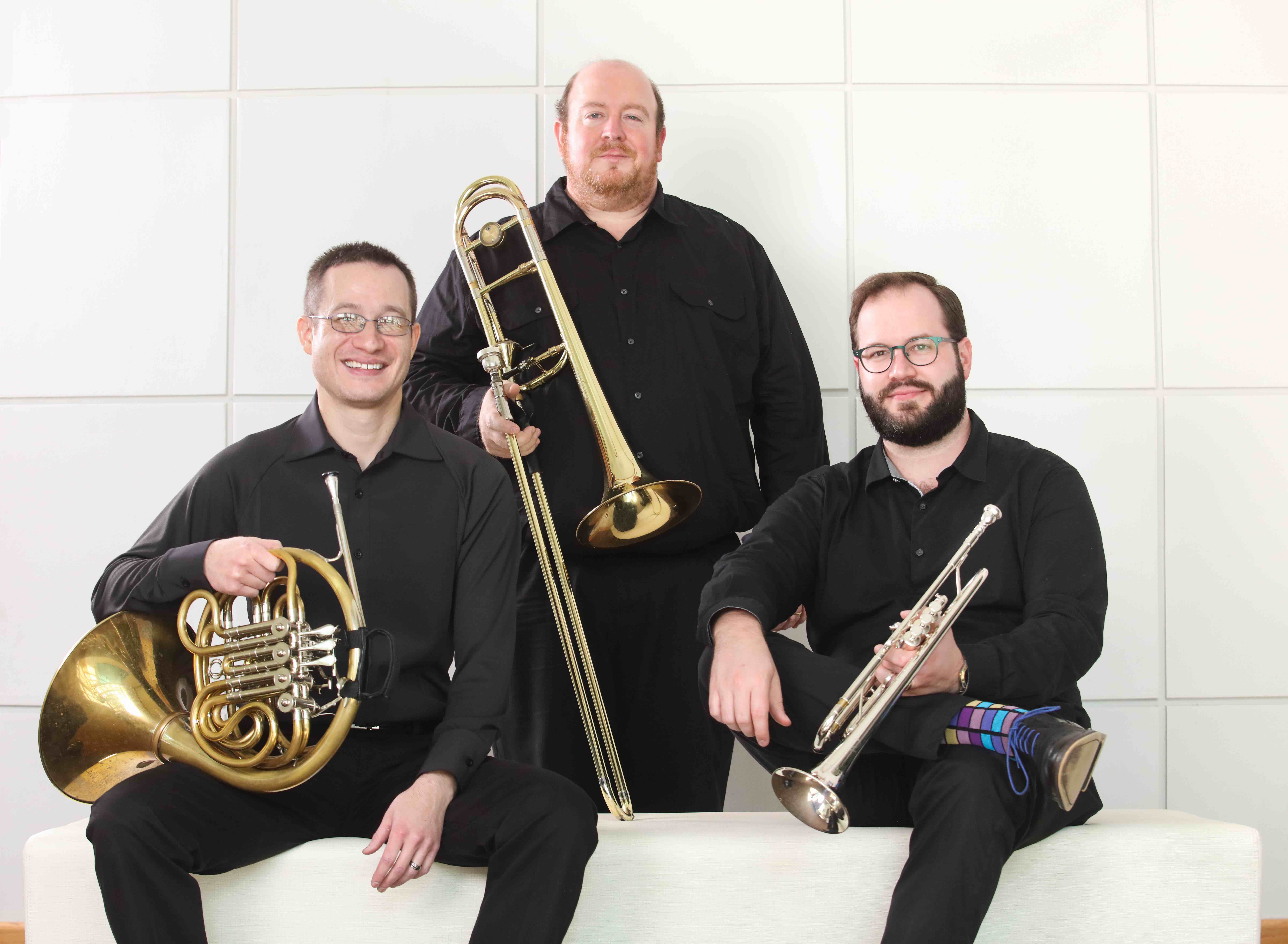 A French horn player, trombone player and trumpet player wearing all black clothes on a white background.