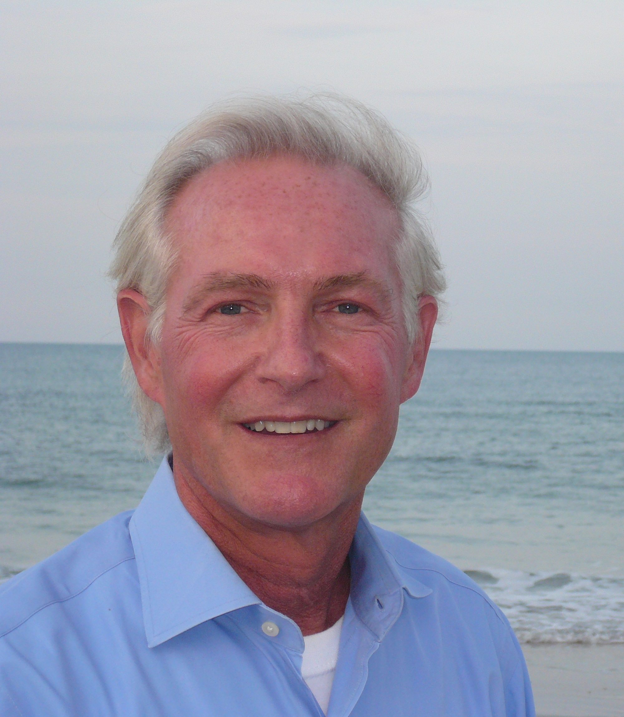 Composer Zack Browning is standing in front of the ocean on a beach.