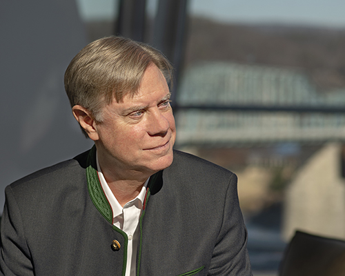 Composer Douglas Hedwig is seated and wearing a brown jacket.