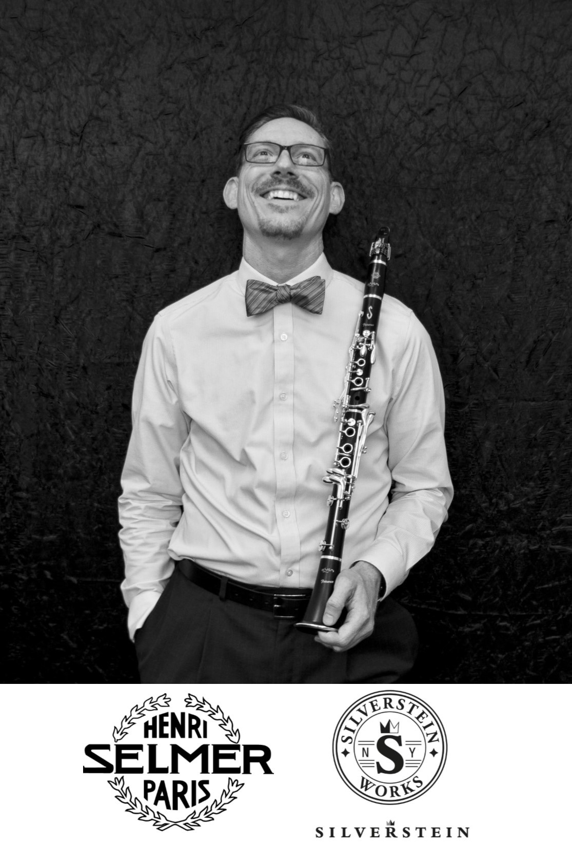 Scot Humes is holding a clarinet and looking up. He is wearing glasses and dress shirt with a bow tie. The Henri Selmer Paris and Silverstein Works logos are pictured below.