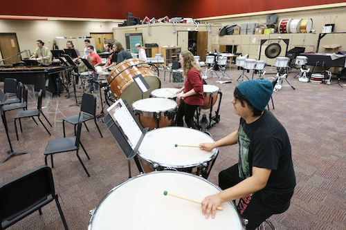 A ULM percussion student wearing a blue hat is playing two timpani drums in the band building.