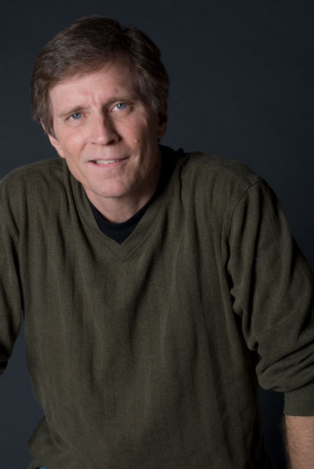 Composer Frank Ticheli is seated and wearing a gray shirt.