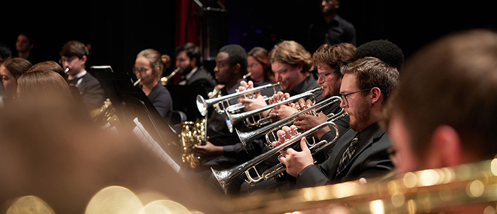 Trumpet and French horn players performing on stage in Brown Auditorium, dressed in black.