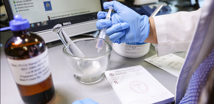 Decorative image of gloved hand dispensing liquid into mortar in the COP mock pharmacy area