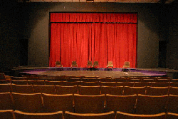 A view of the stage in Spyker Theatre looking from the audience. A red curtain is on stage.